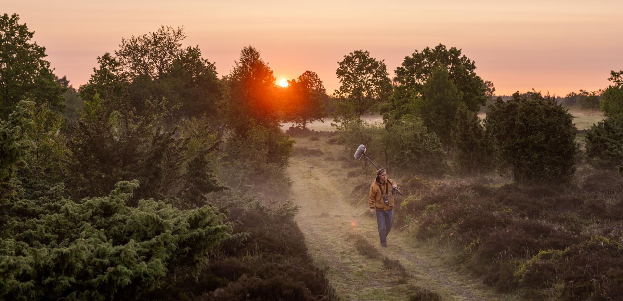 A man walking down a  road next to a forest.