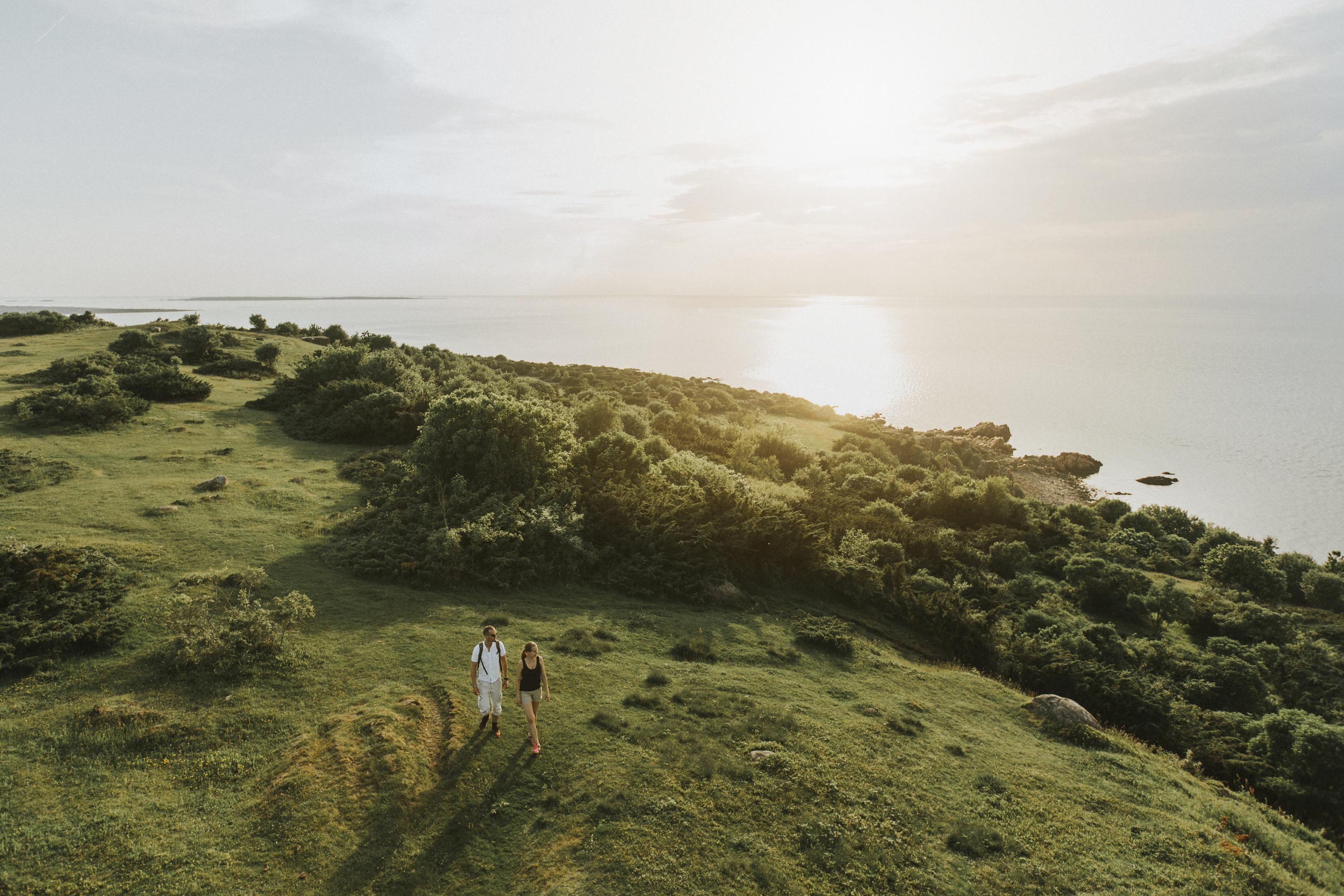 Ett par fotvandrar på ett grönt landskap med havet i bakgrunden i Hovs Hallar