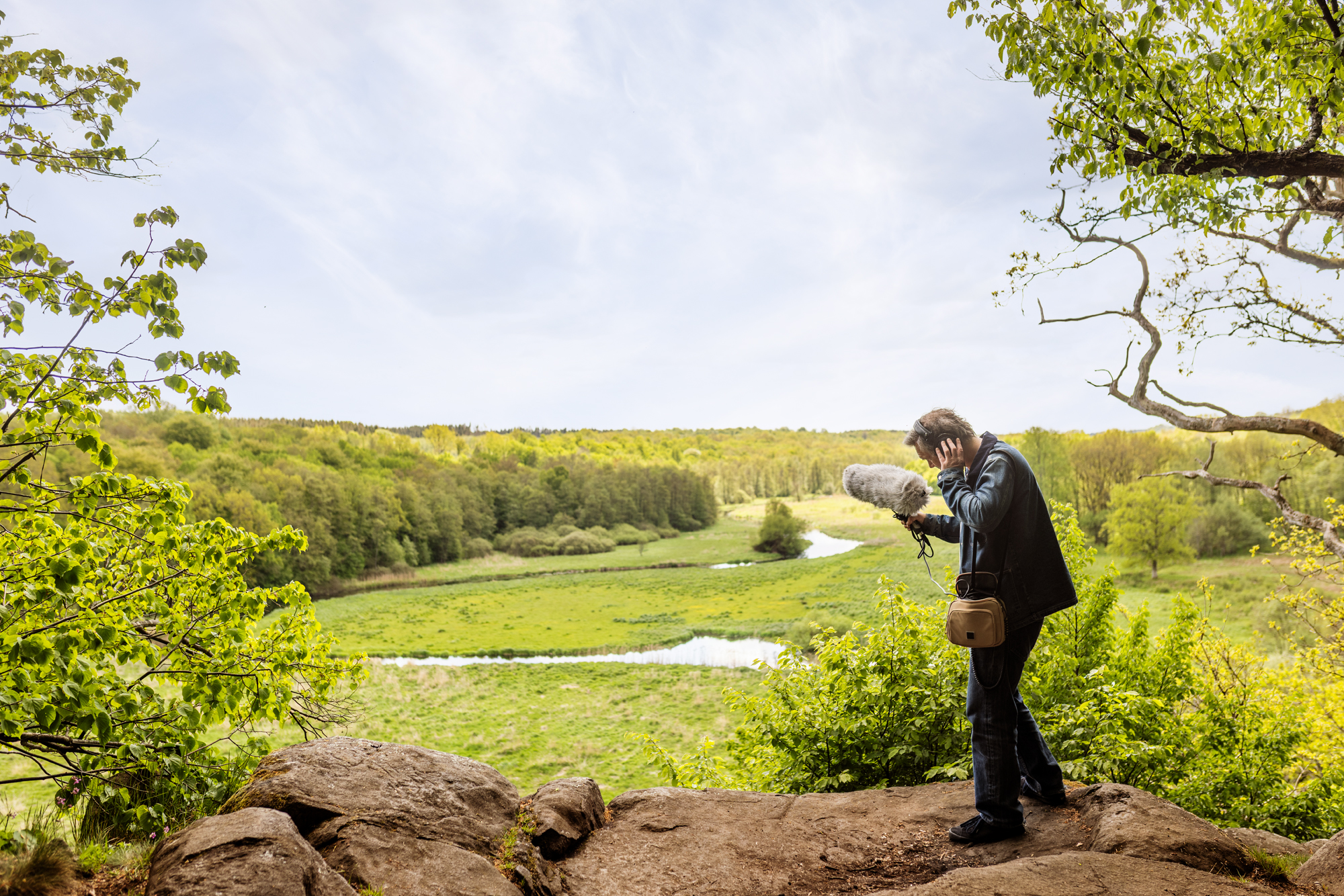 A man standing on top of a rock next to a lush green field and river.