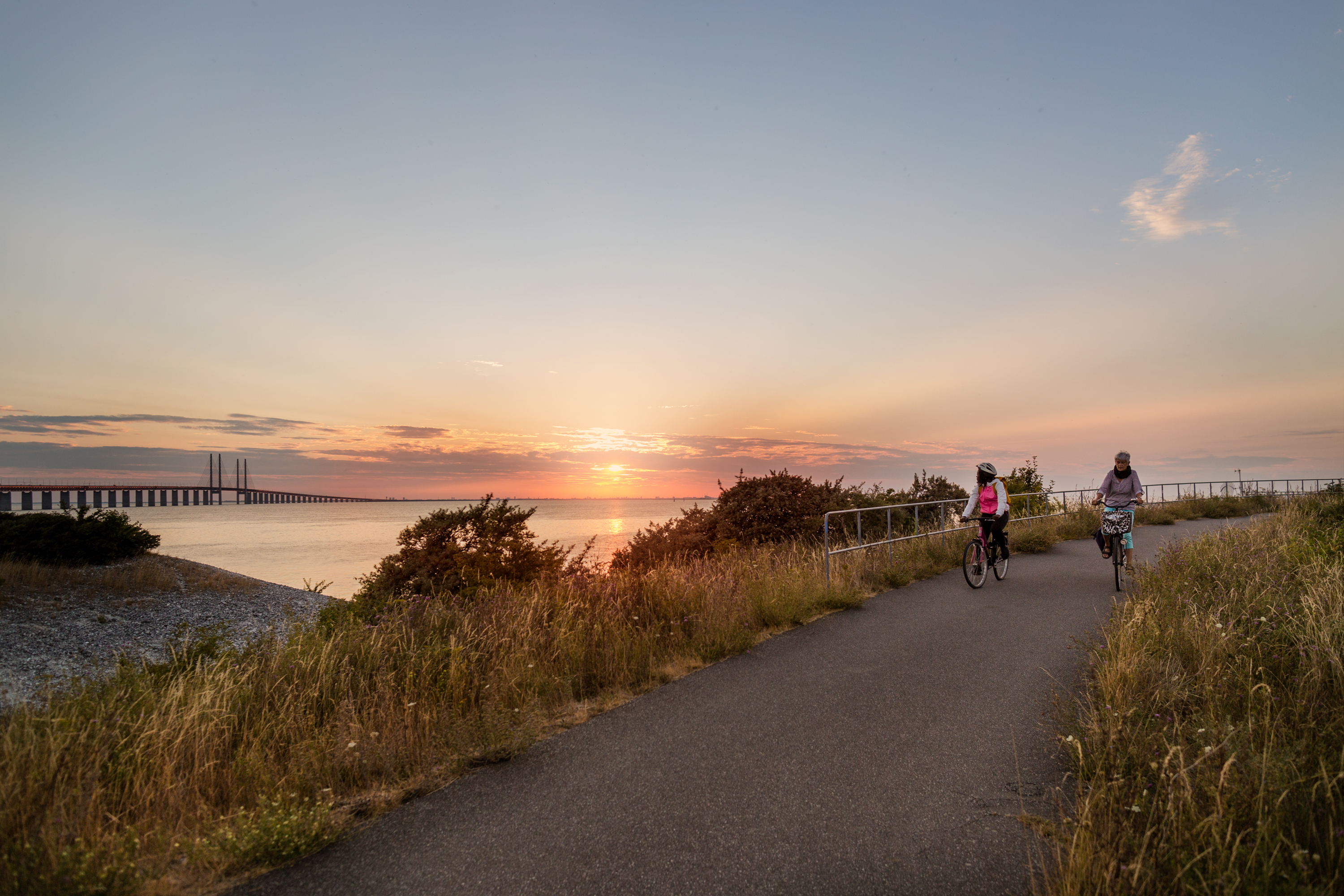 A sunset over Öresund with two people biking