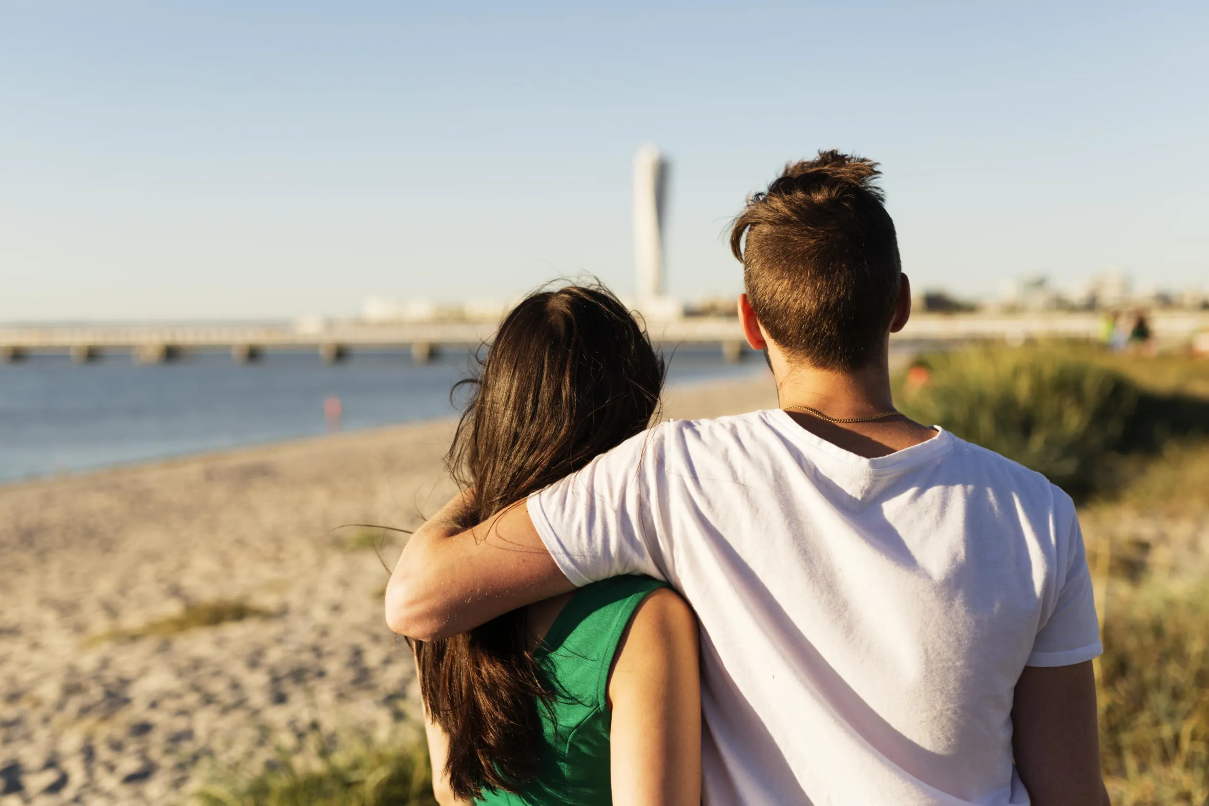 Ein Paar steht am Strand von Ribersborg und blickt auf den langen Steg zum Badehaus und den Wolkenkratzer Turning Torso.