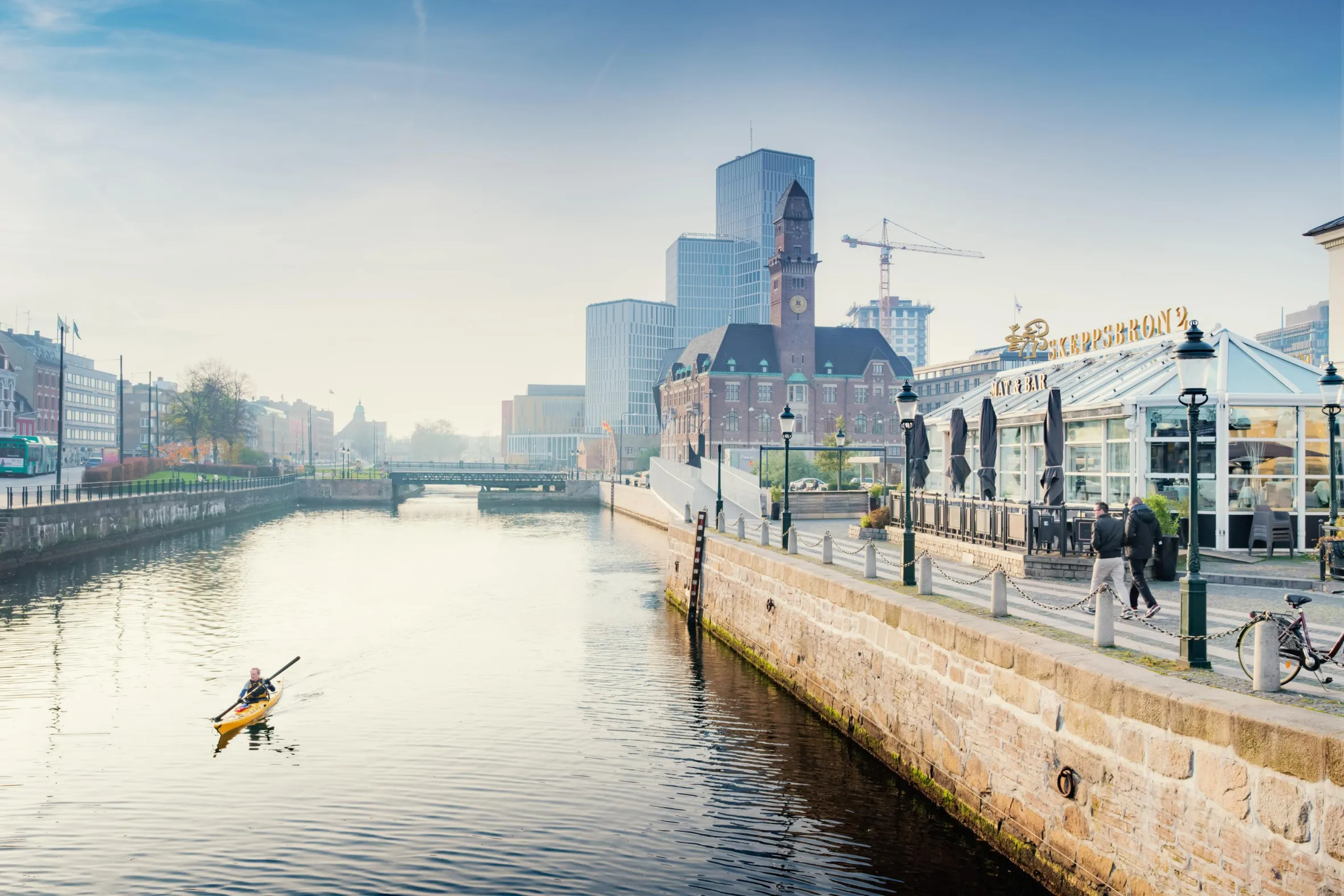 A person kayaks in the Malmö canal, with Malmö Live in the background.
