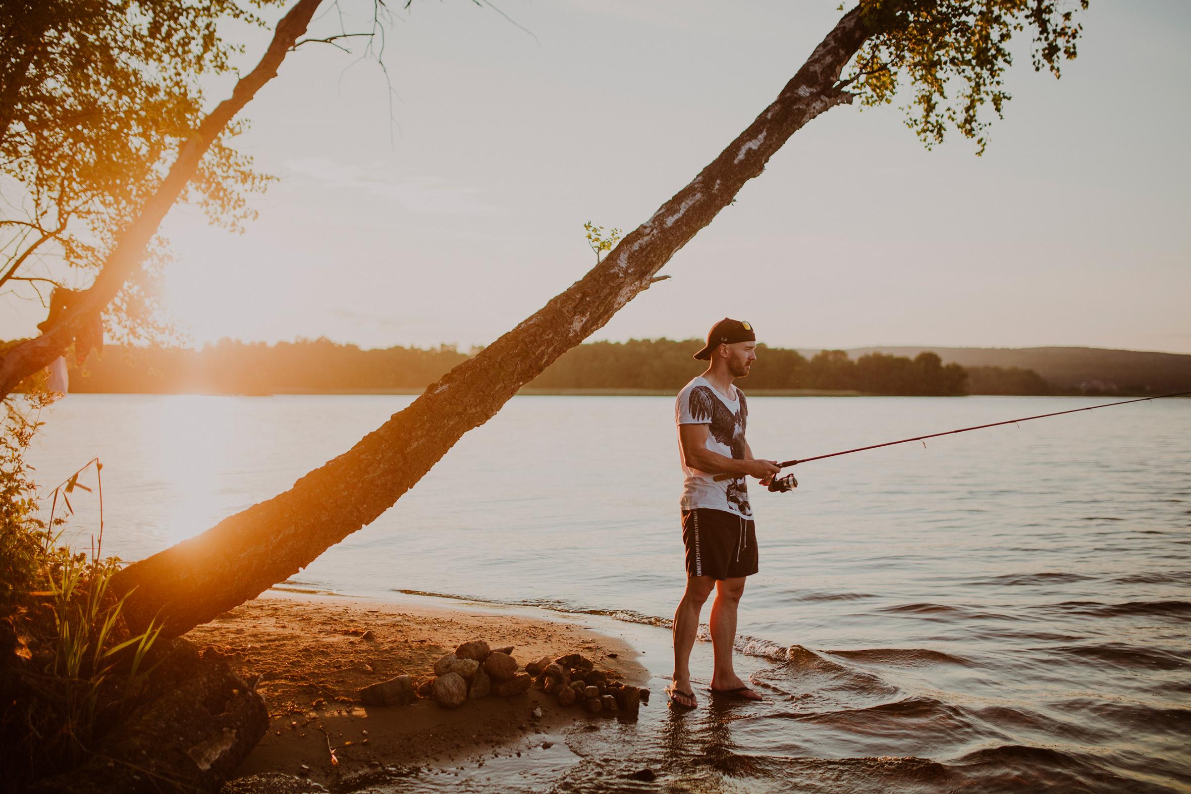 En man som står på stranden på Ivösjön och fiskar vid solnedgången