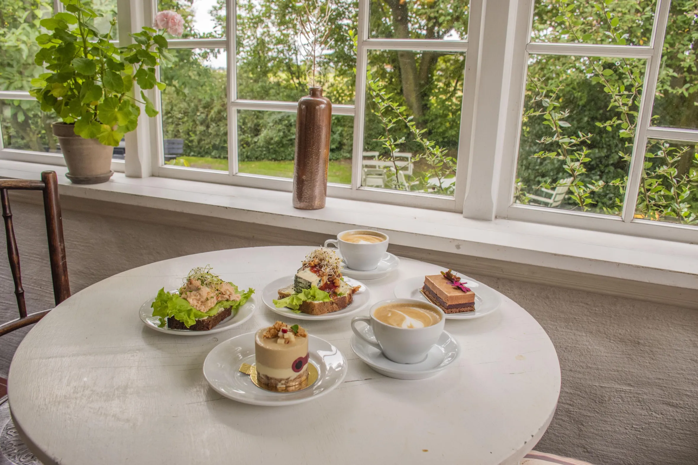 Ett bord med utplacerade smörgåsar, bakverk och kaffe med utsikt över trädgården