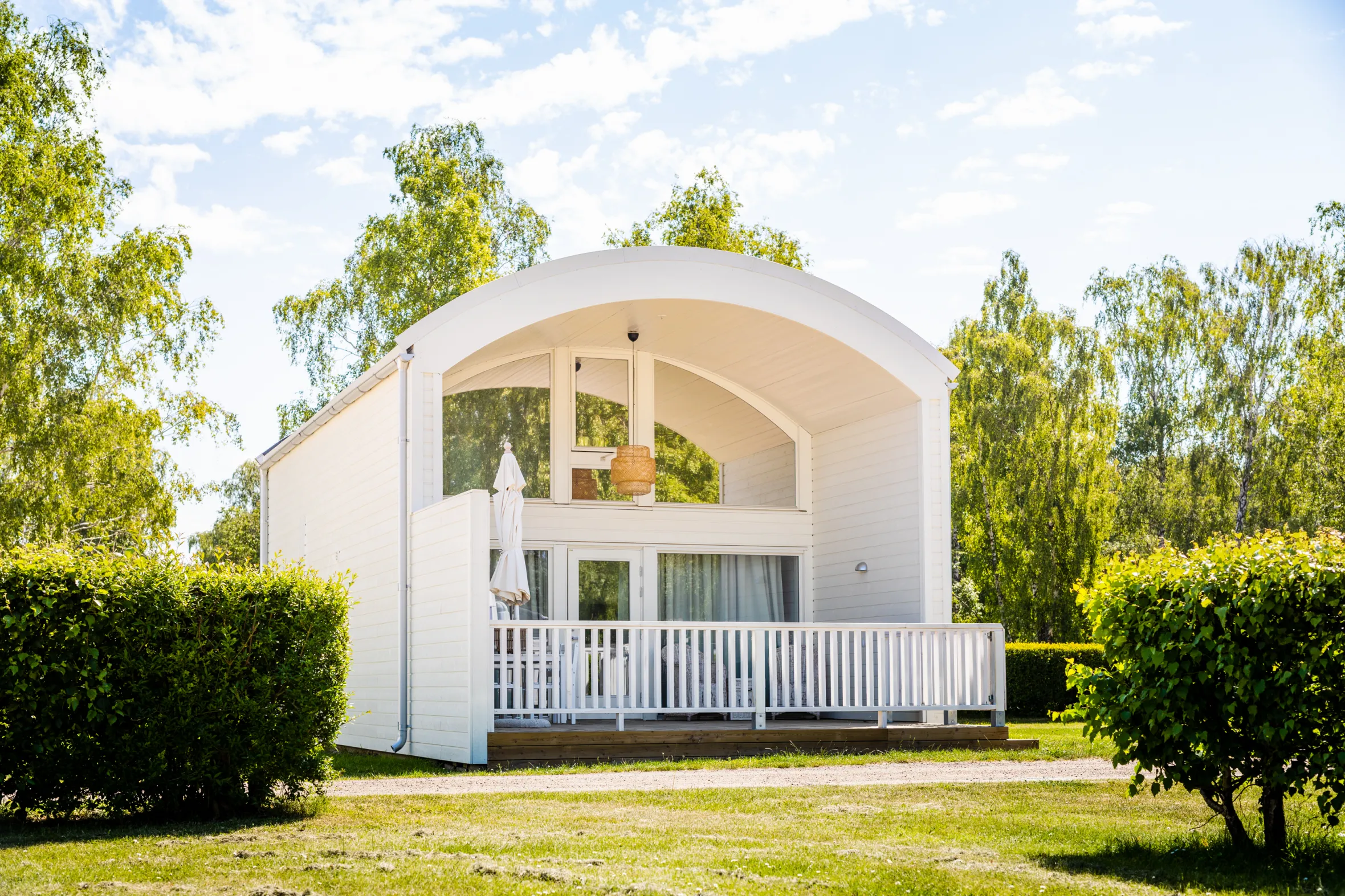 A white cottage with vaulted roof and terrace with lawn and shrubs in front