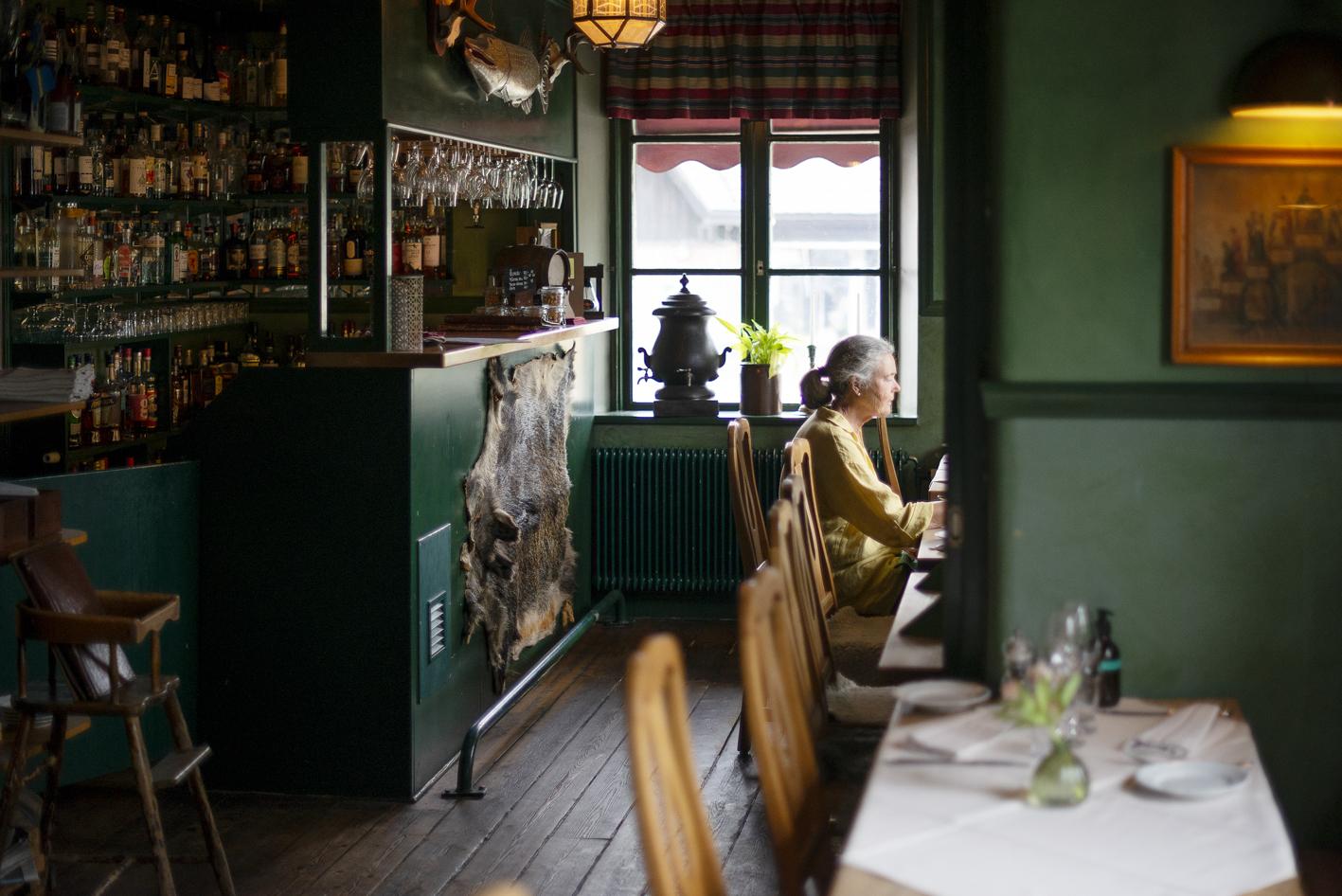 Traditional inn with green walls and an elderly woman sitting by a table