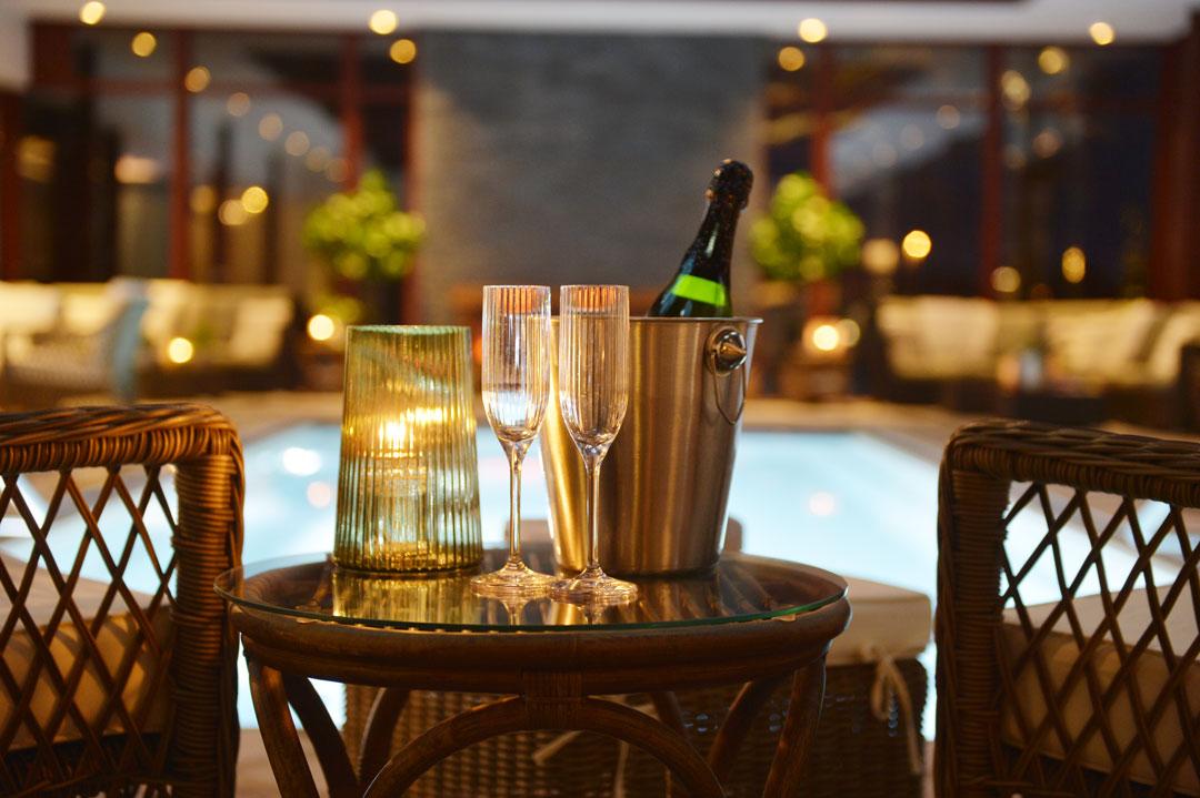 Two chairs and a table with flute glasses and a bottle in front of a pool