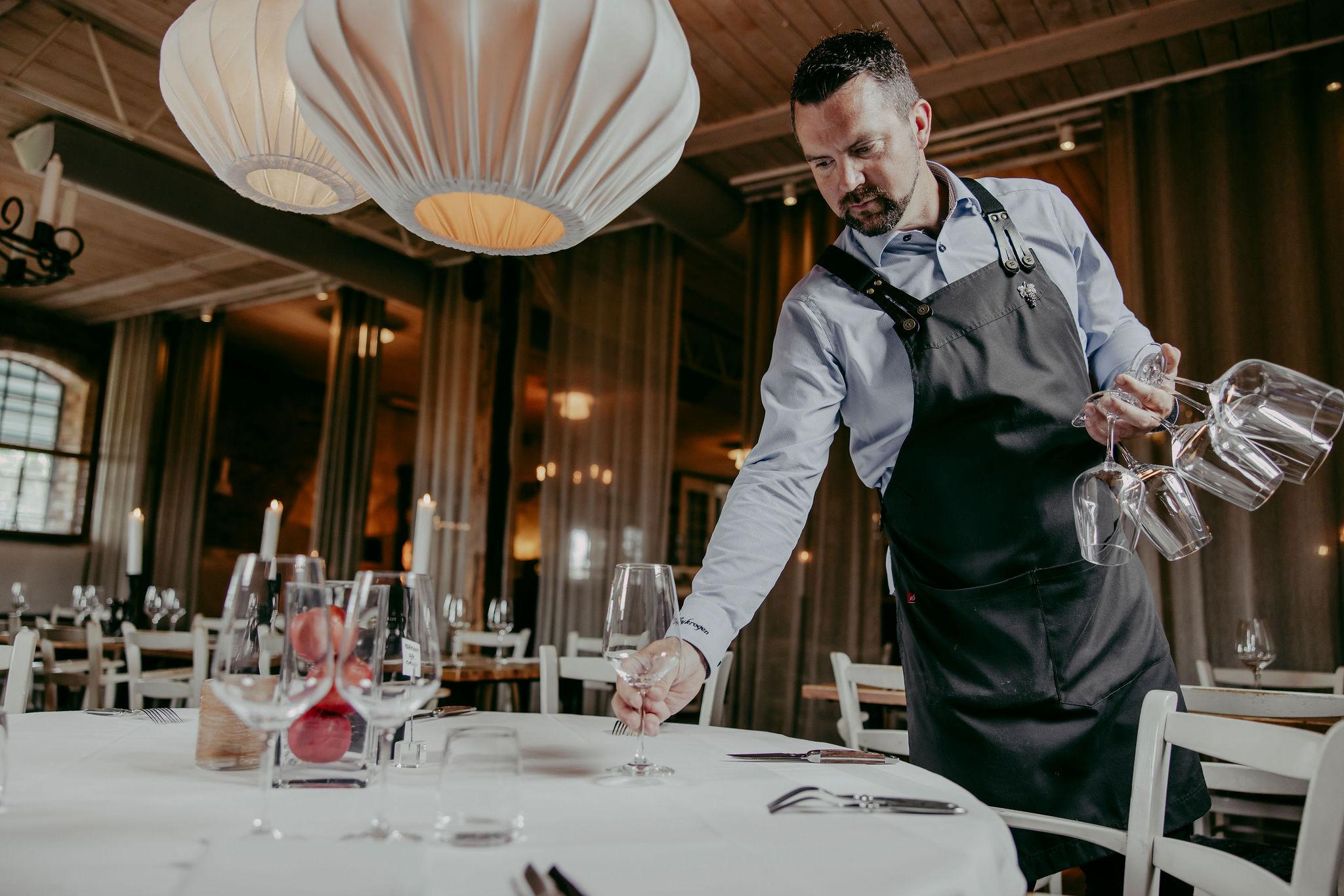 Male waiter sets a table with wine glasses in a chic restaurant interior