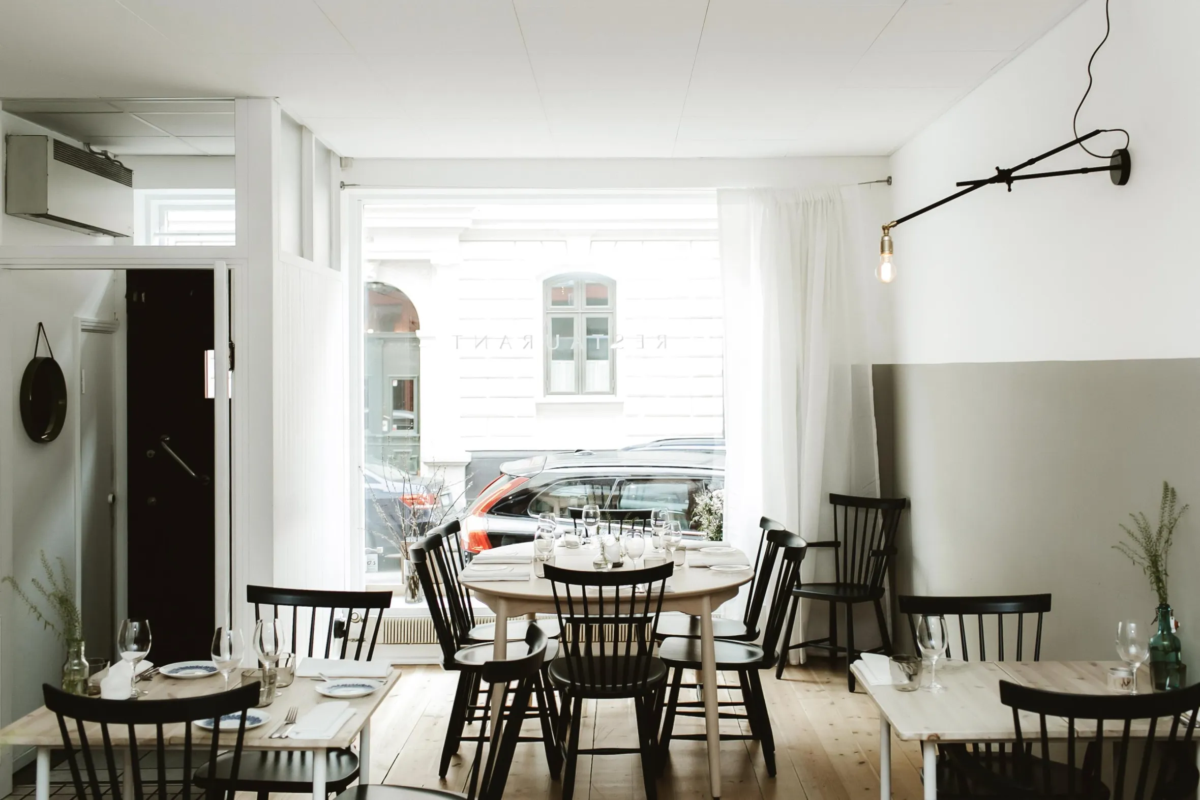 Bright Scandinavian-style restaurant interior featuring minimalist design and large street-facing window revealing urban views