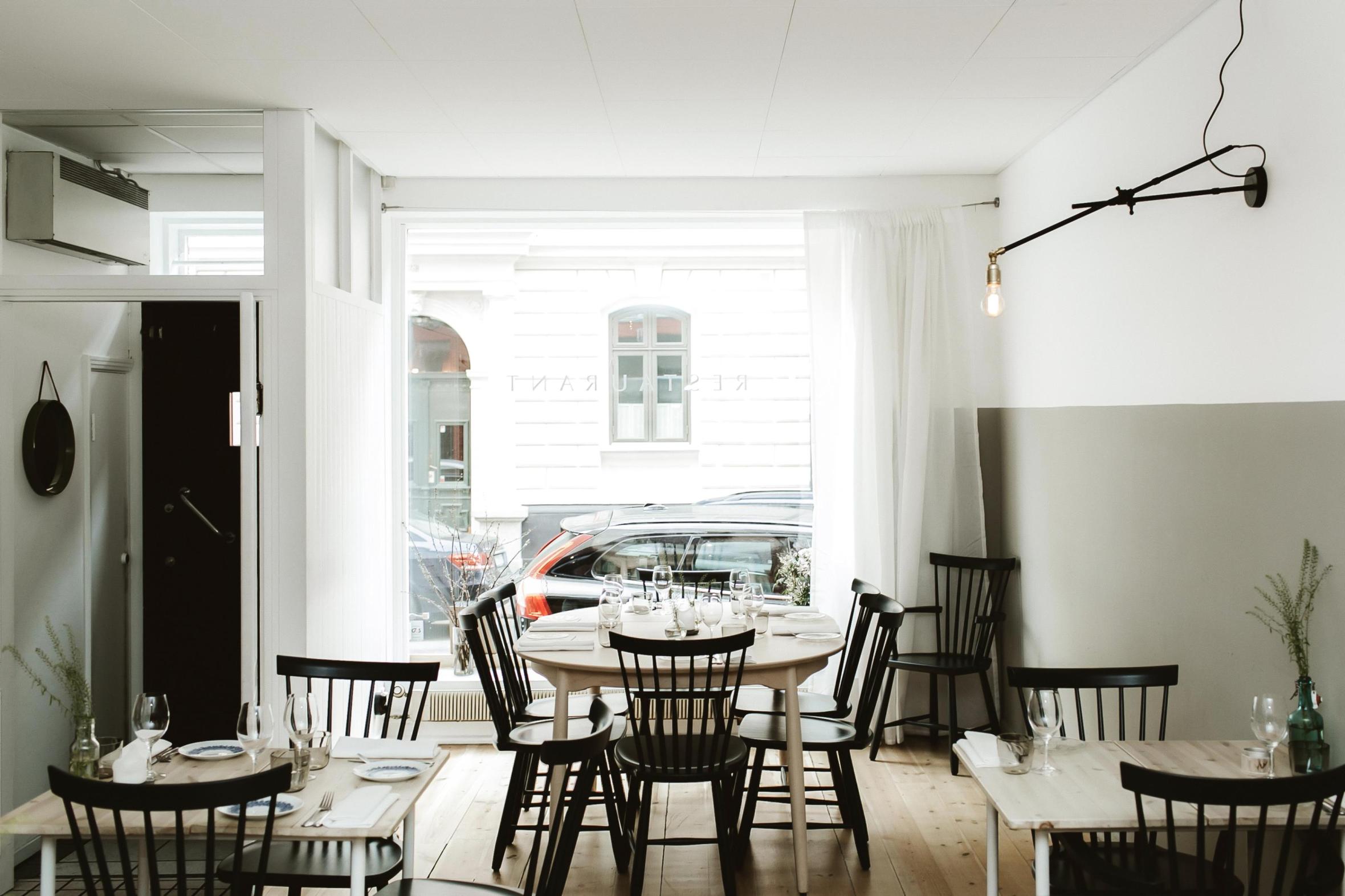 Bright Scandinavian-style restaurant interior featuring minimalist design and large street-facing window revealing urban views