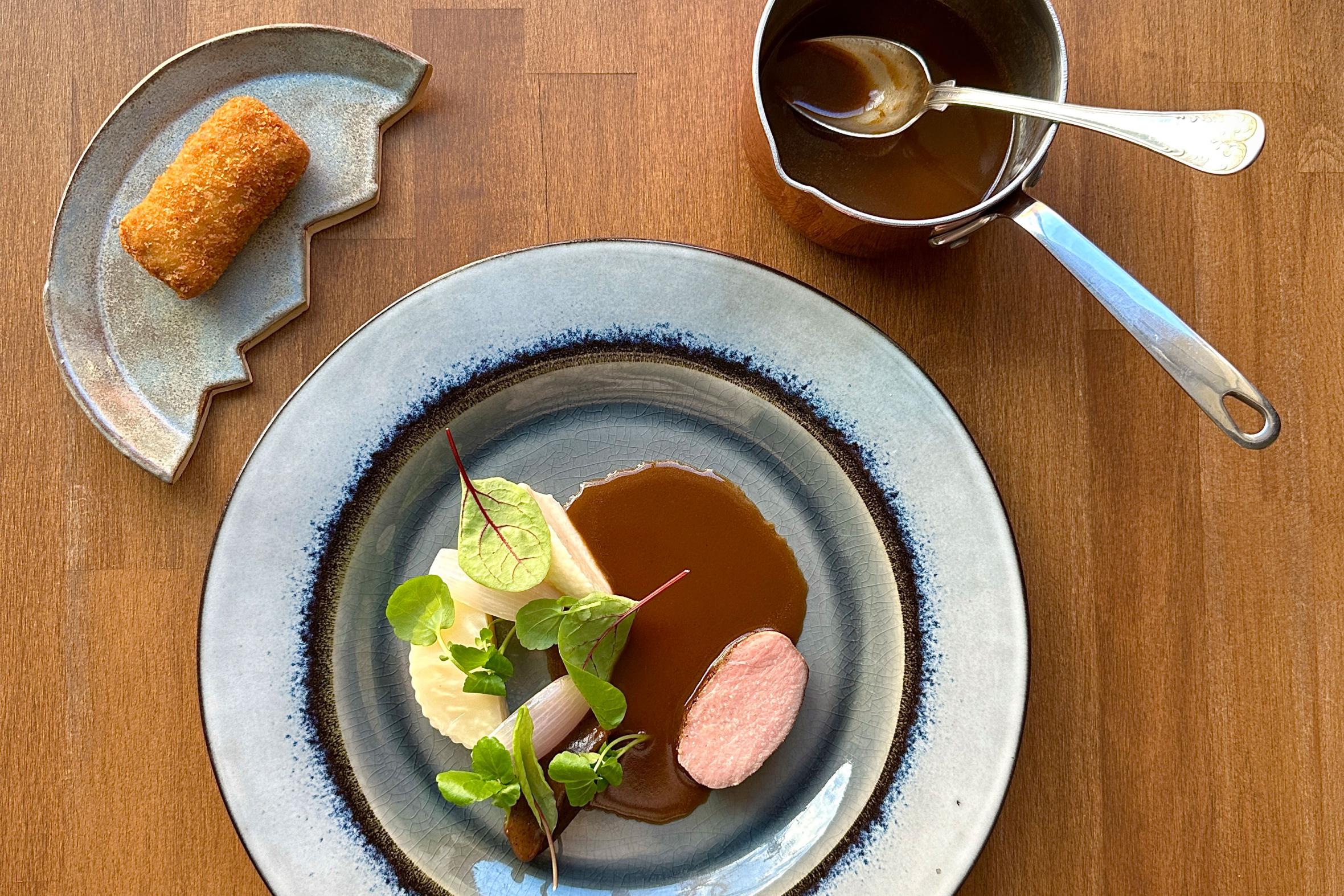 Plated meat dish with potato puree and sauce, garnished with herbs, served with side croquette and separate sauce boat