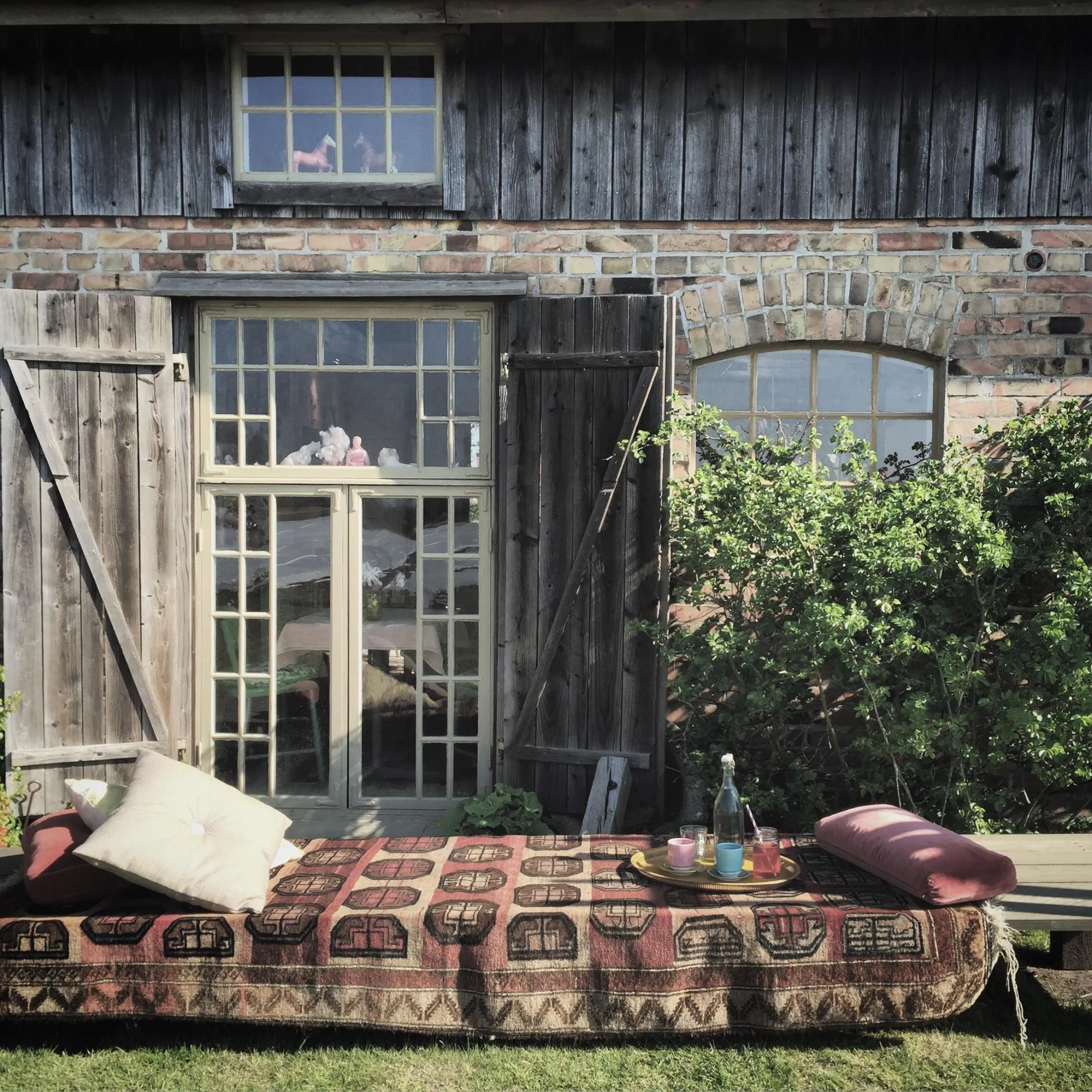 Inviting coffee bench with blanket and pillow in front of a wall of an old building
