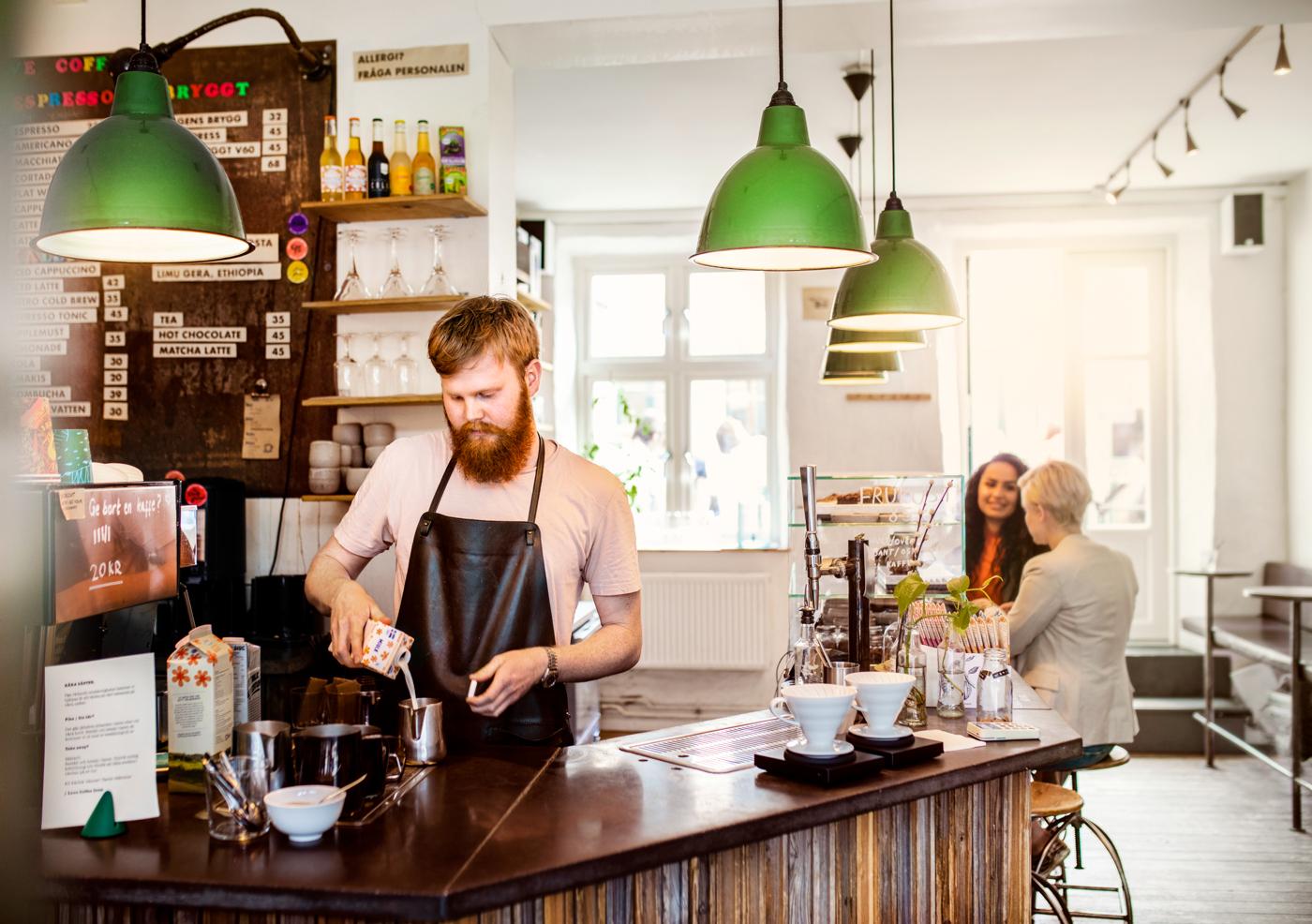 Manlig barista förbereder kaffe bakom en bar med gröna lampor i taket