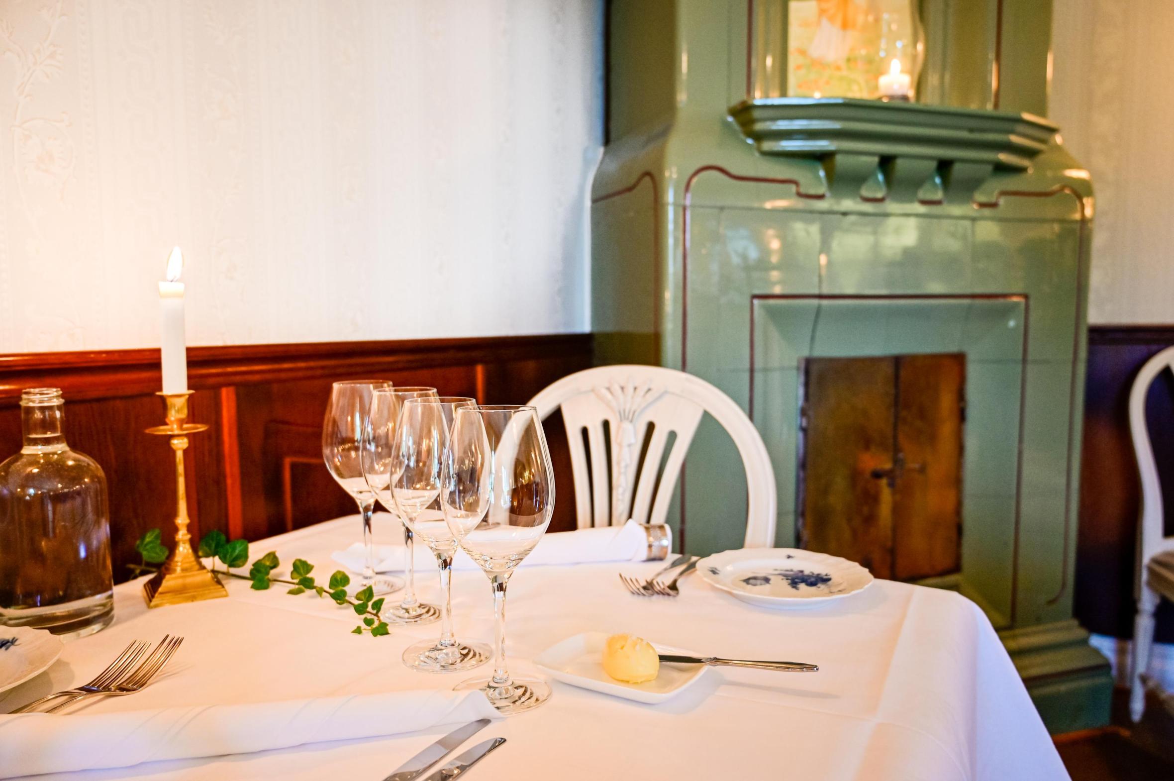 Formal table setting with elegant stemware in a row, ivy branch centerpiece and tiled stove visible in background