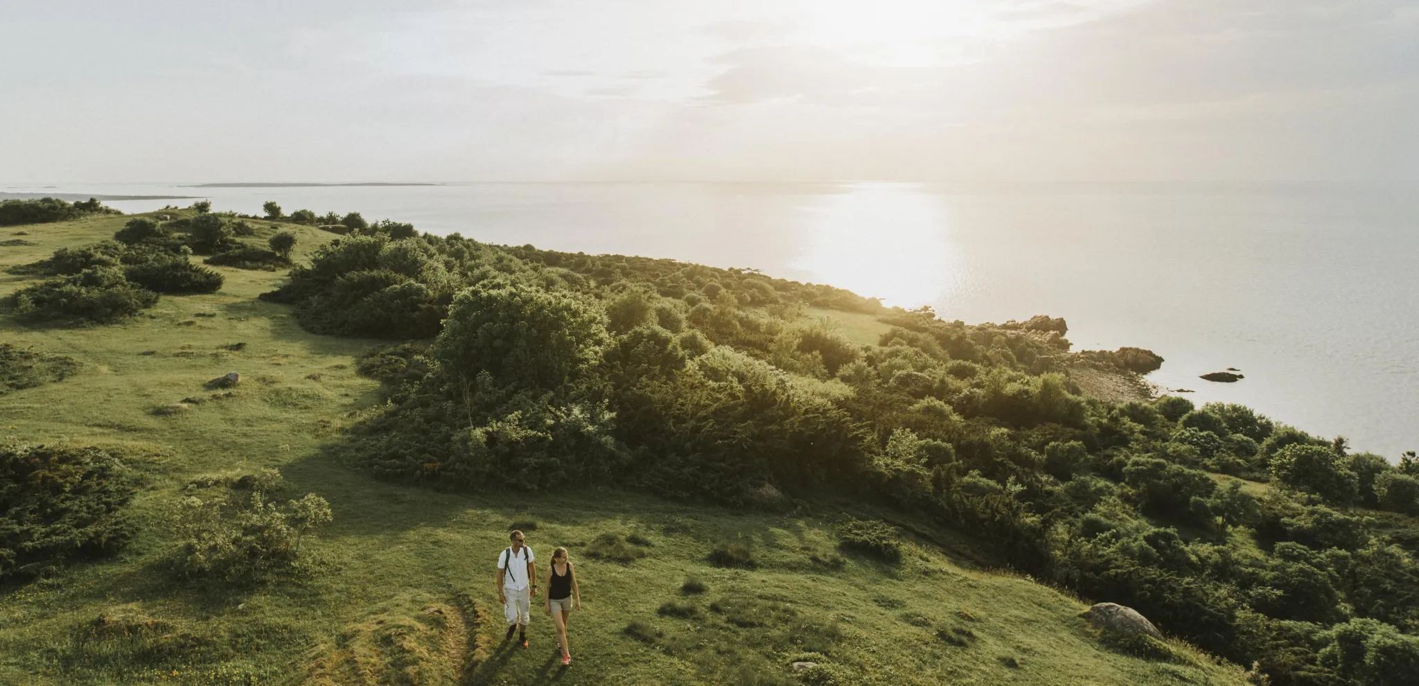 Ett par fotvandrar på ett grönt landskap med havet i bakgrunden i Hovs Hallar