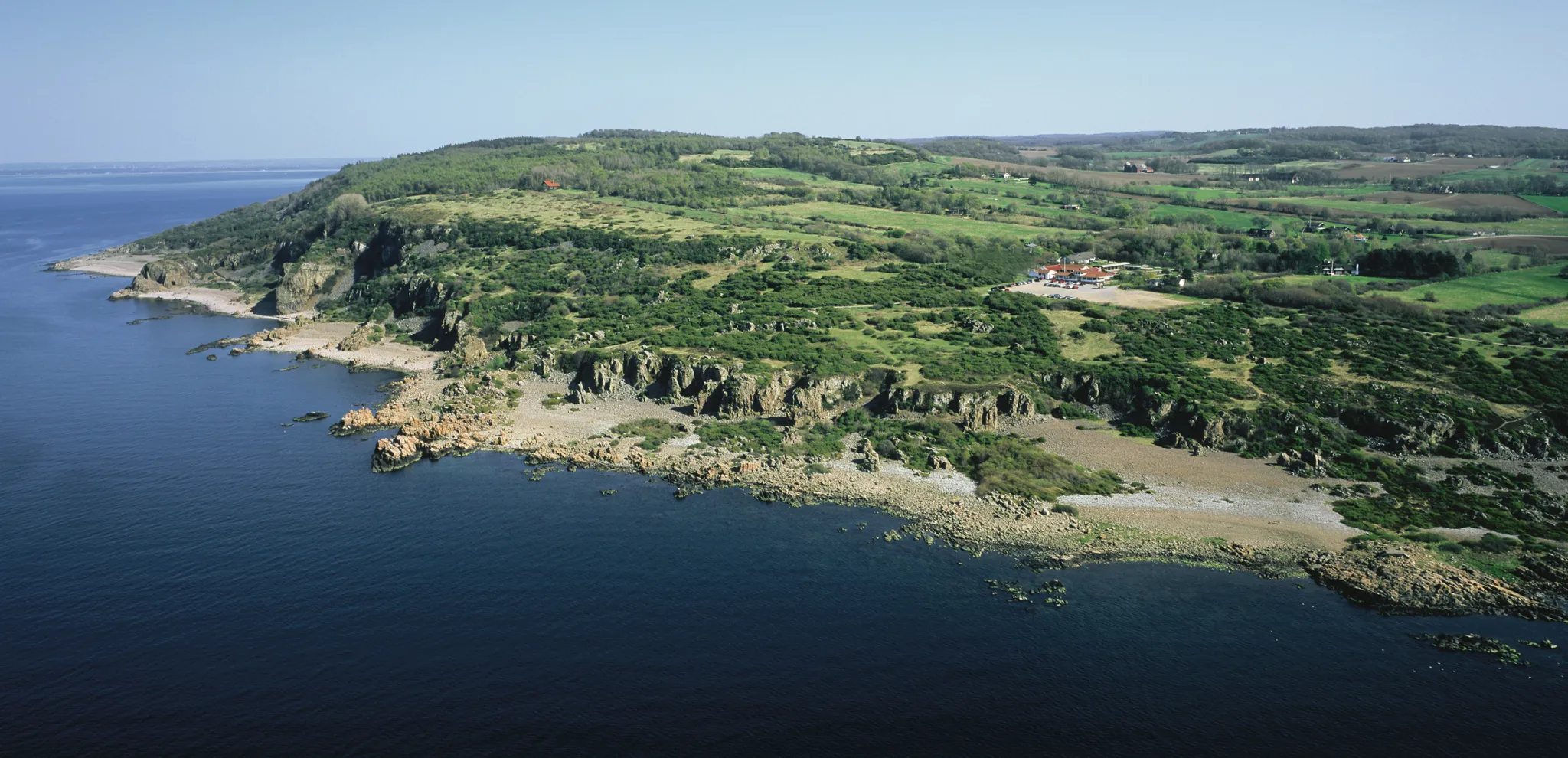 Drone view of a coastline with steep cliffs and green countryside 