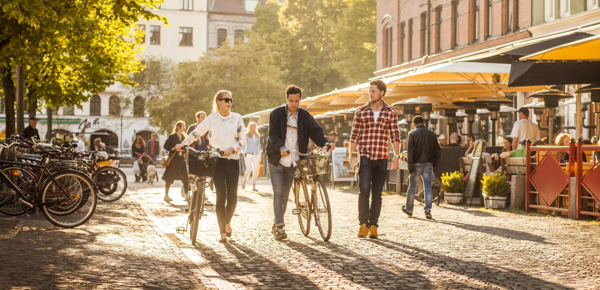  People walking with bikes in the summer at Möllvången's square in Malmö