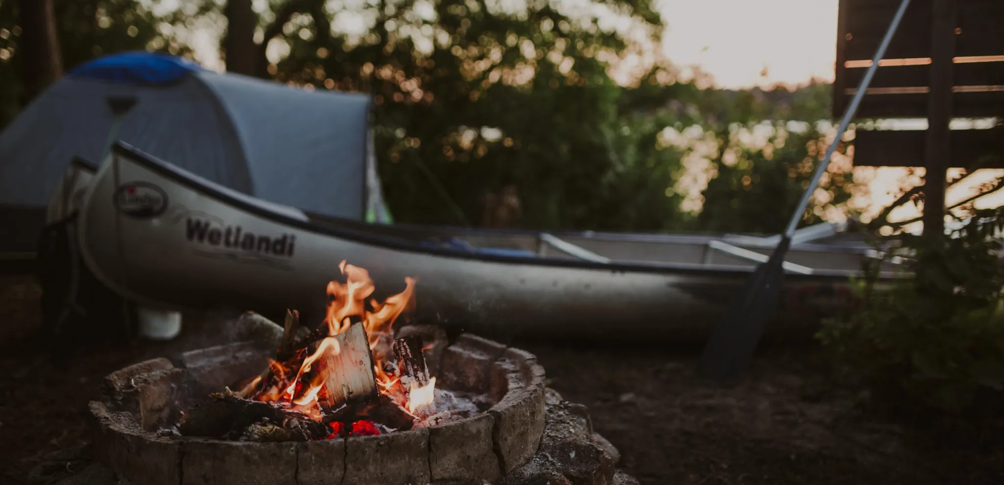 A campsite with a campfire and canoe by Lake Ivösjön