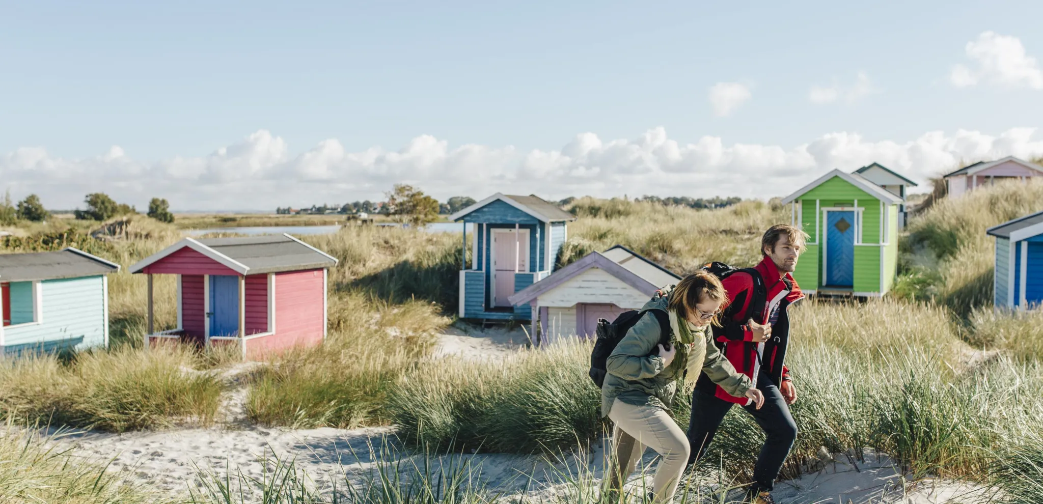 Couple hiking on sandunes with beach cabins 