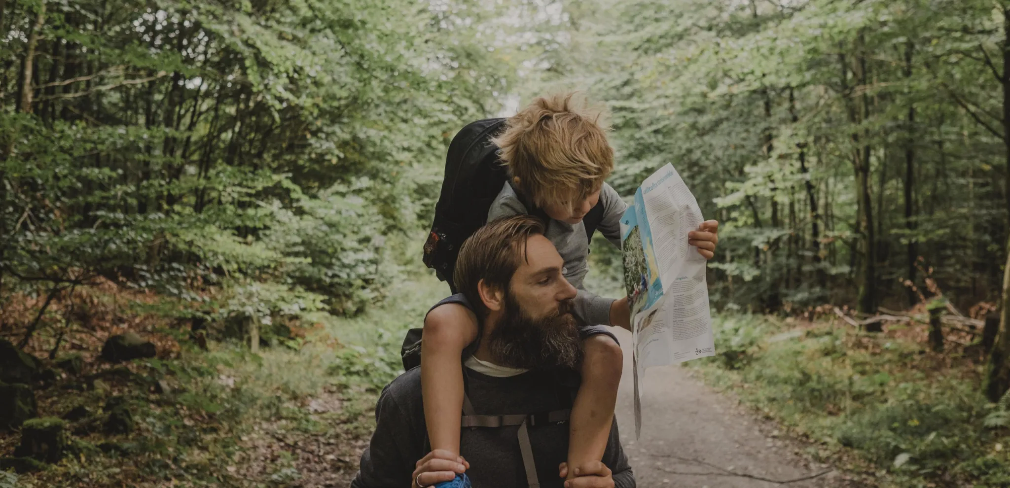 Father with his child on his shoulders in nature surroundings looking at a map 
