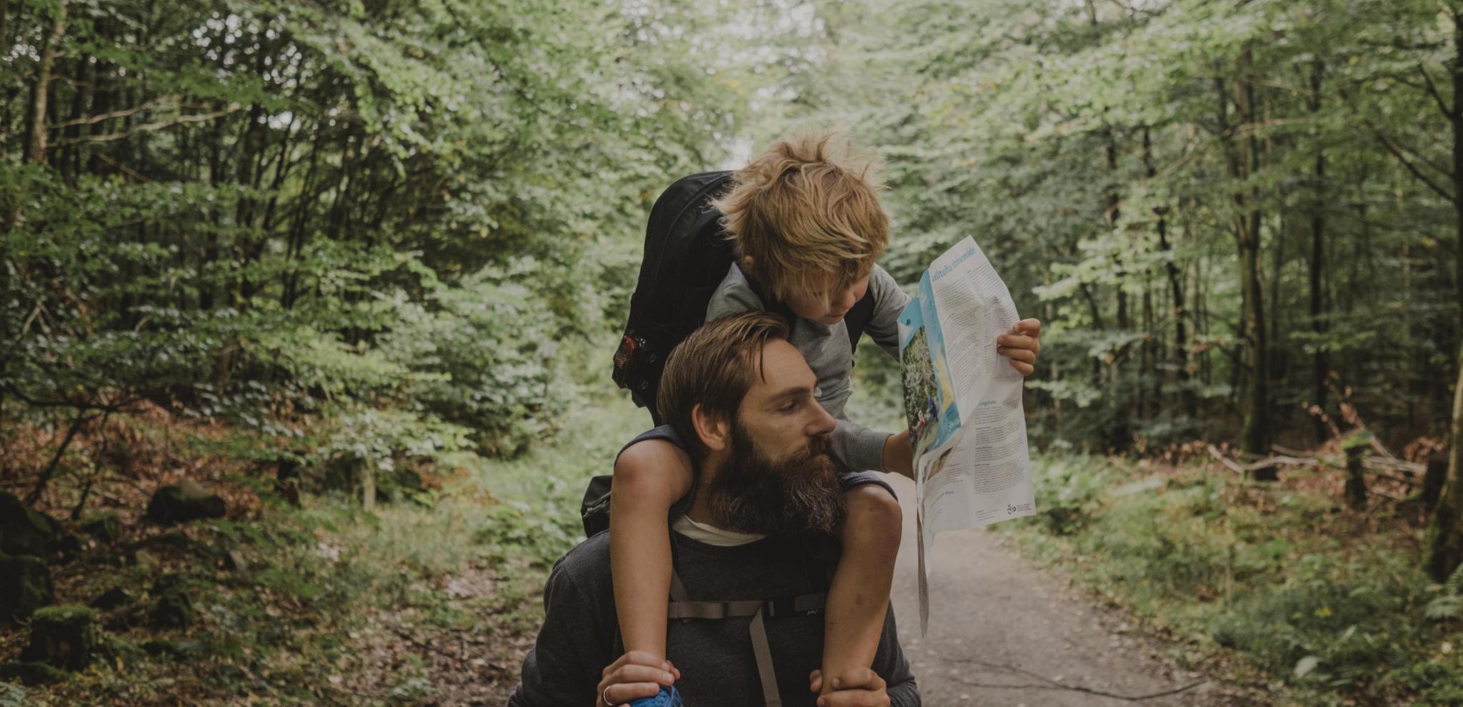 Father with his child on his shoulders in nature surroundings looking at a map