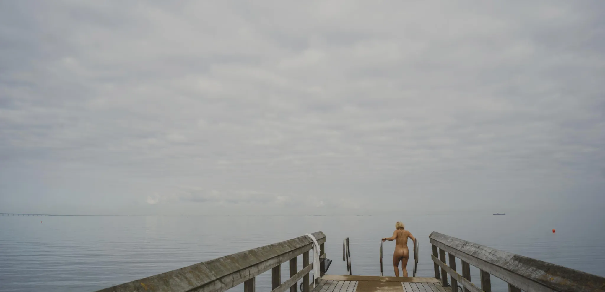 Naked woman walking down pier stairs to bathe