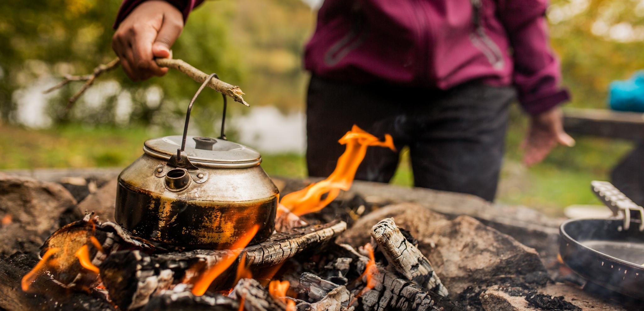 A person heats a teapot over an open fire