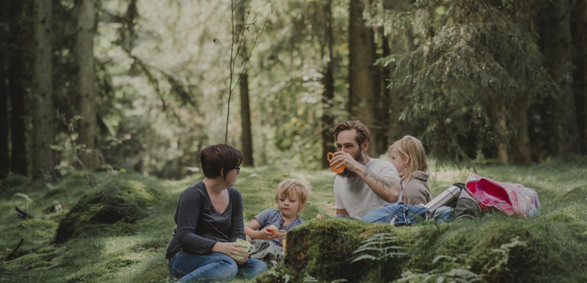 Familj med mamma pappa och två barn fikar i skogen