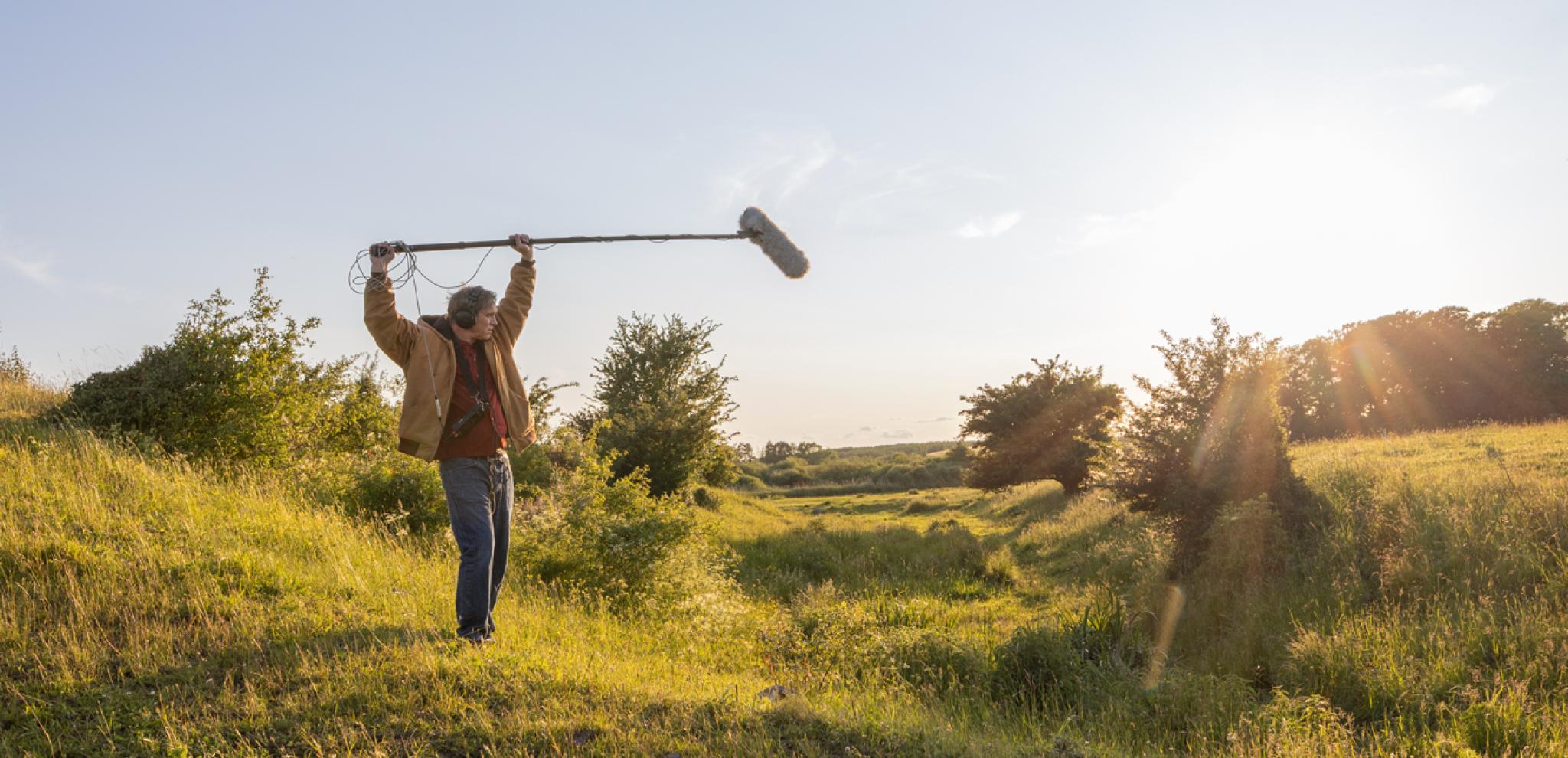 A man holding a microphone on top of a lush green field.