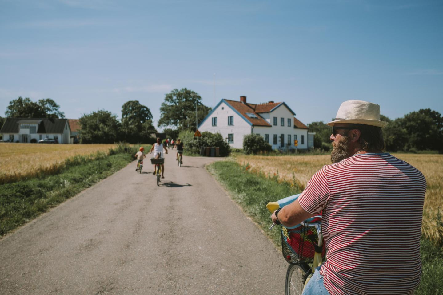 Family biking through the fields on a gravel road towards a white house on the island of Ven