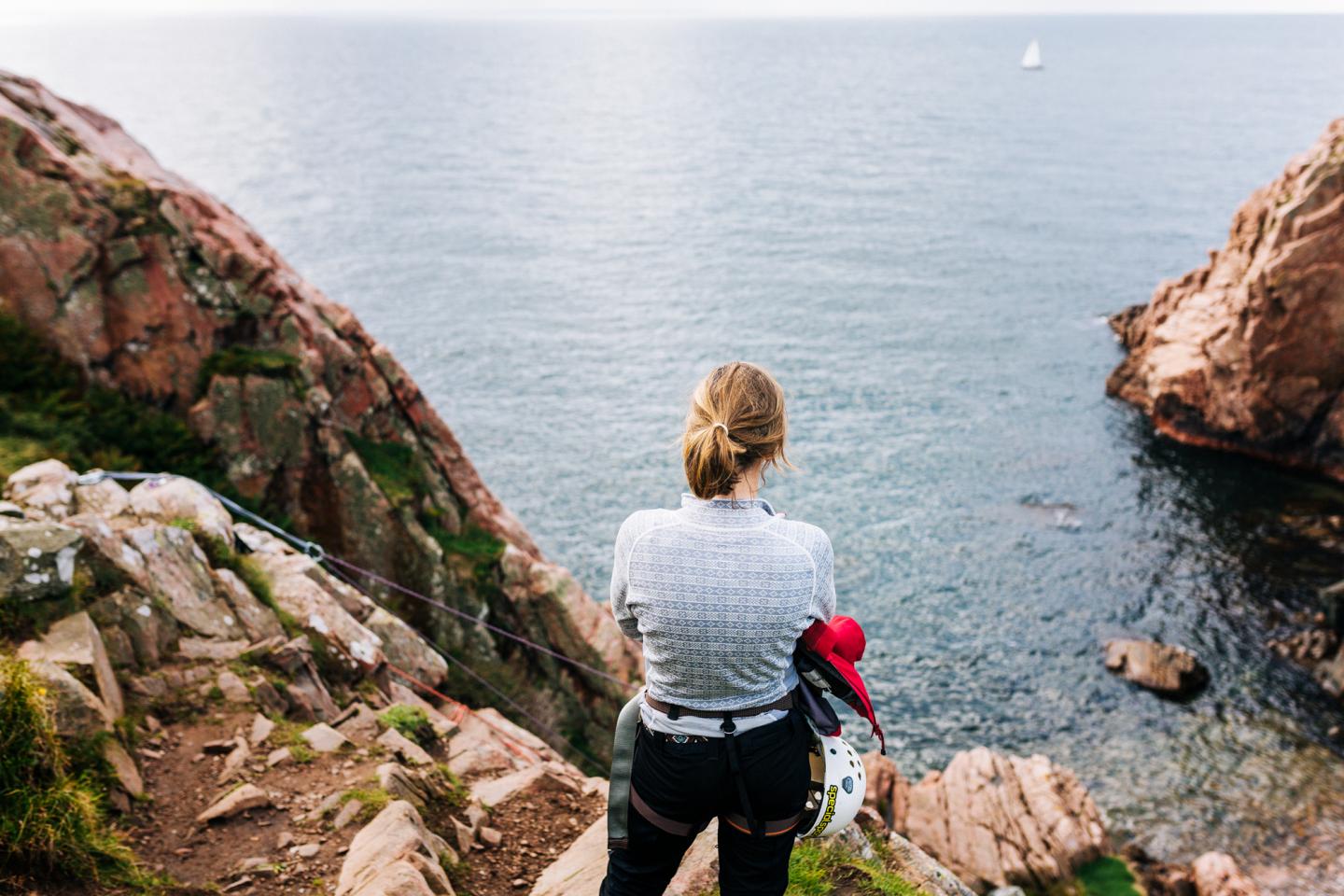 A woman climbing on top of a cliff looking down at the sea in Kullaberg