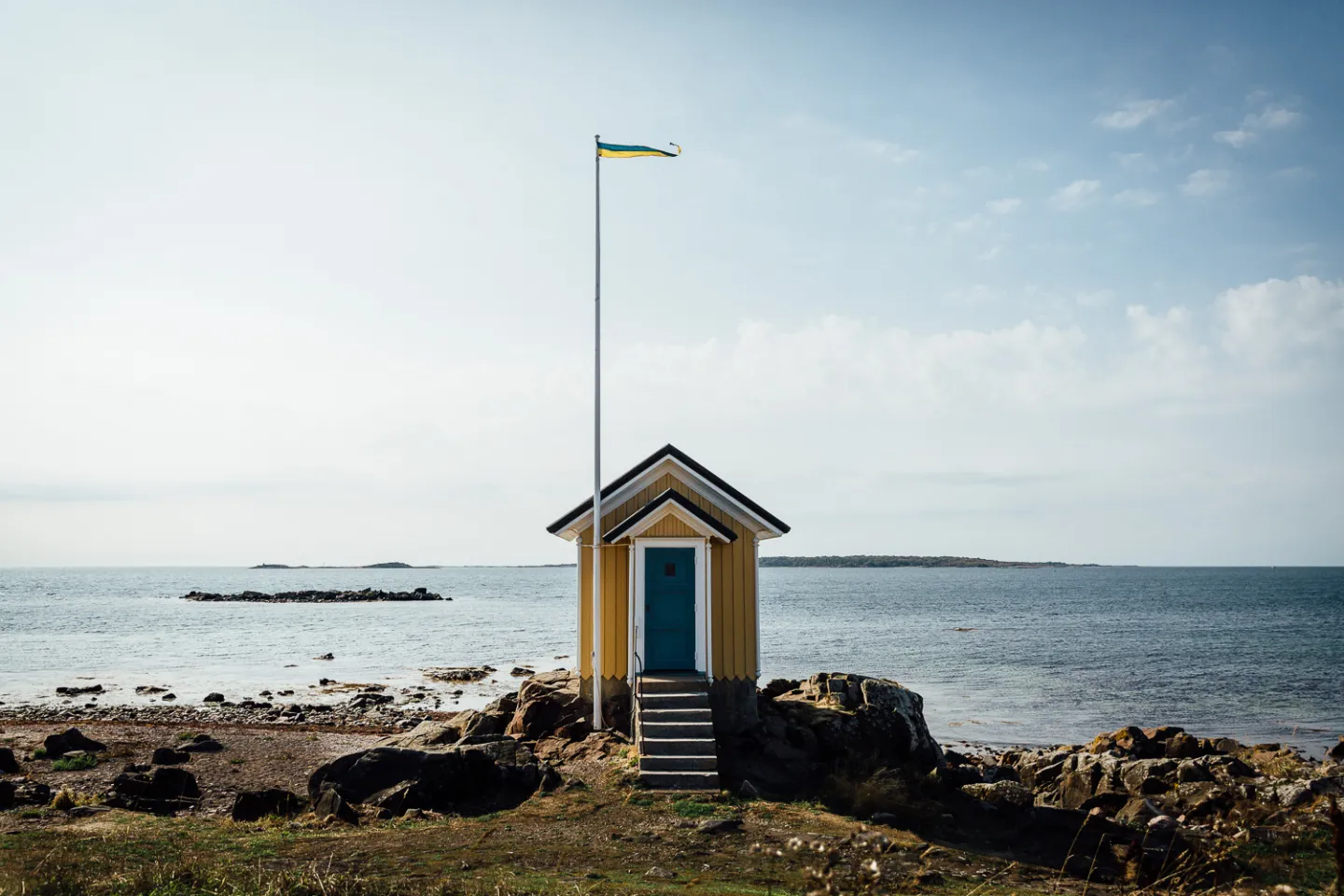 En liten gul stuga vid stranden med havet- och ett fartyg i bakgrunden