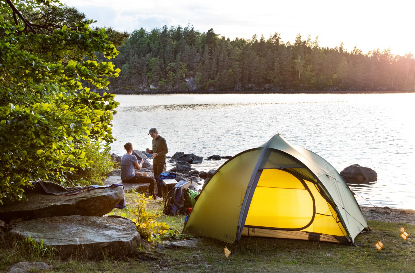 Ein Paar hat am Ufer eines Sees inmitten von Wald ein gelbes Zelt aufgebaut.