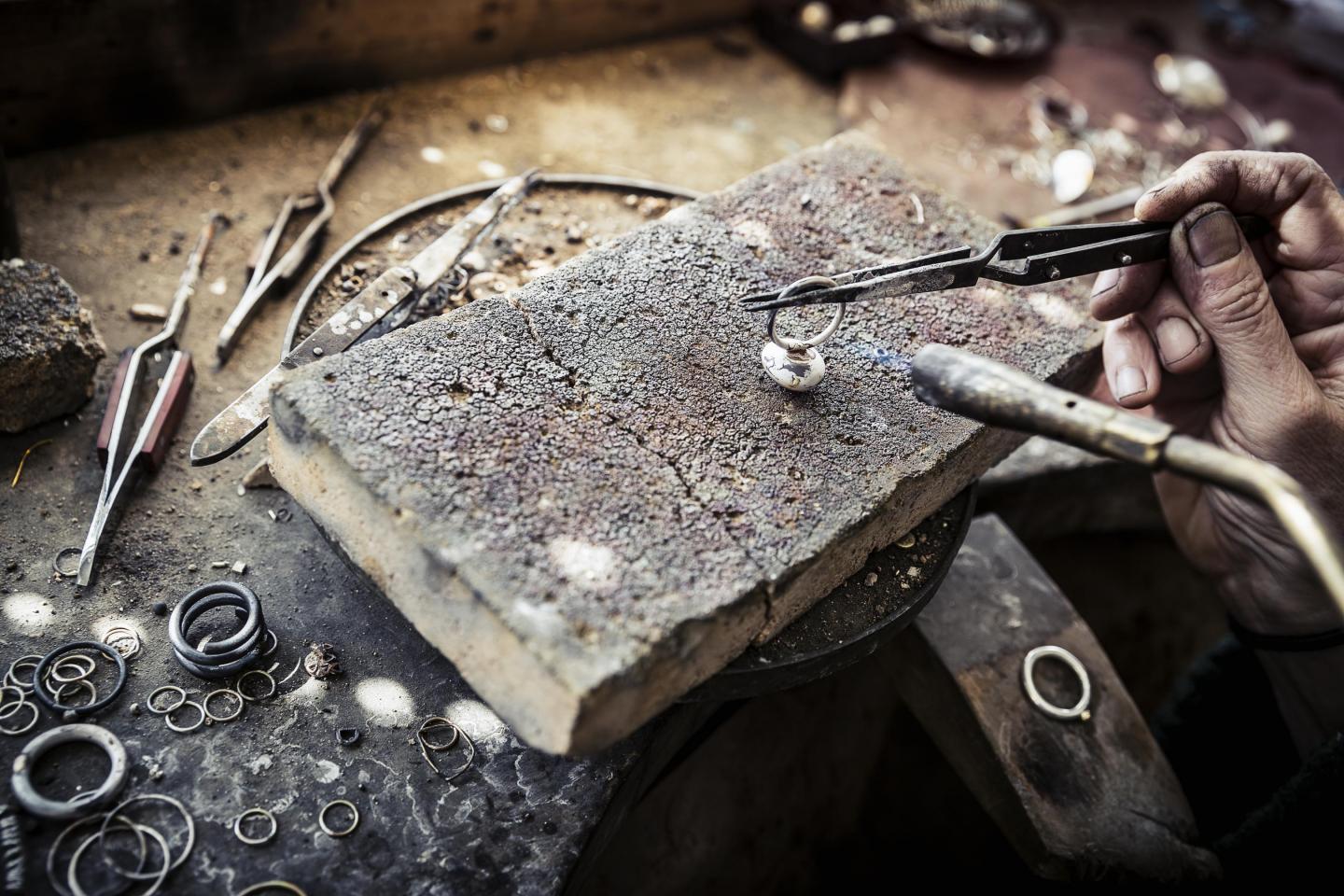 Ein Silberschmied fertigt an seinem Arbeitstisch mit Werkzeugen einen Ring.