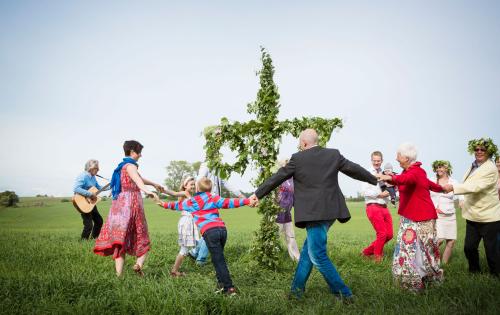 A group of people dancing and singing around the traditional midsummerpole 