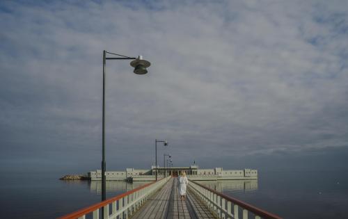 Pier with lampost leading to green open-air bathhouse surrounded by the sea