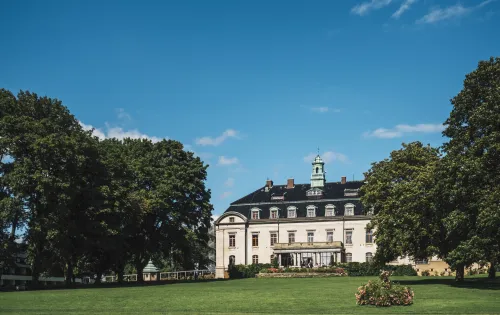 Vitt slott med stor gräsmatta framför och stora träd på sidorna