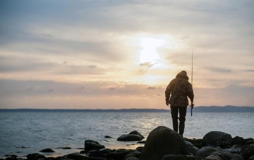 En man som ska fiska bland klipporna vid soluppgång