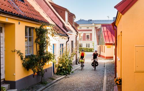  Two cyclists come cycling on a cobbled street among picturesque houses.