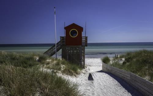 Wooden lifeguard tower with circular window on sandy beach path through dunes, overlooking calm blue sea under twilight sky