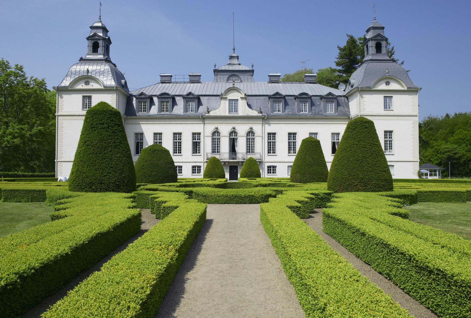 En labyrintträdgårds av buxbom med det sagolika Kronovalls slott i bakgrunden