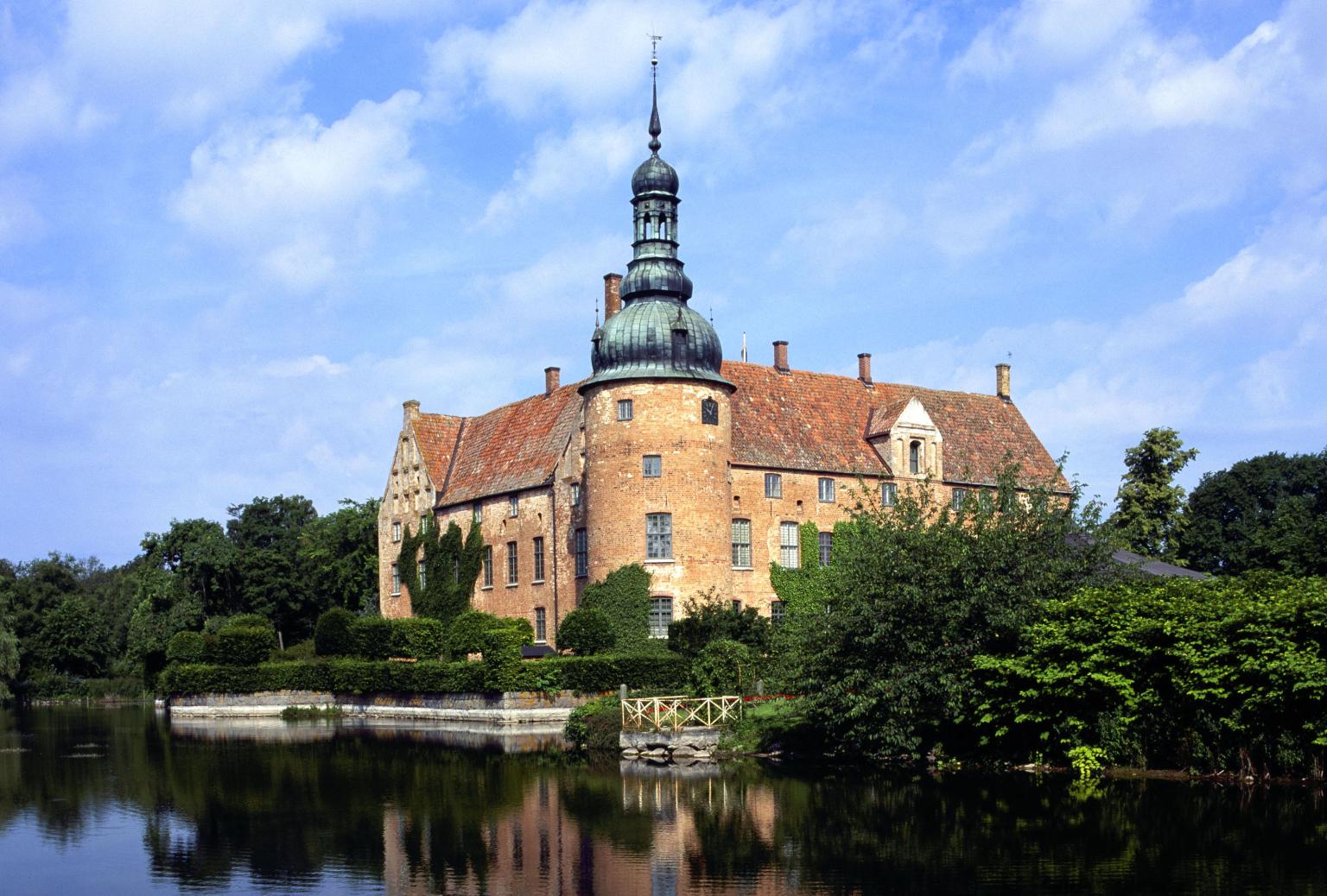 Das Schloss Örenäs im Sommer, umgeben von Natur und einem Wassergraben.