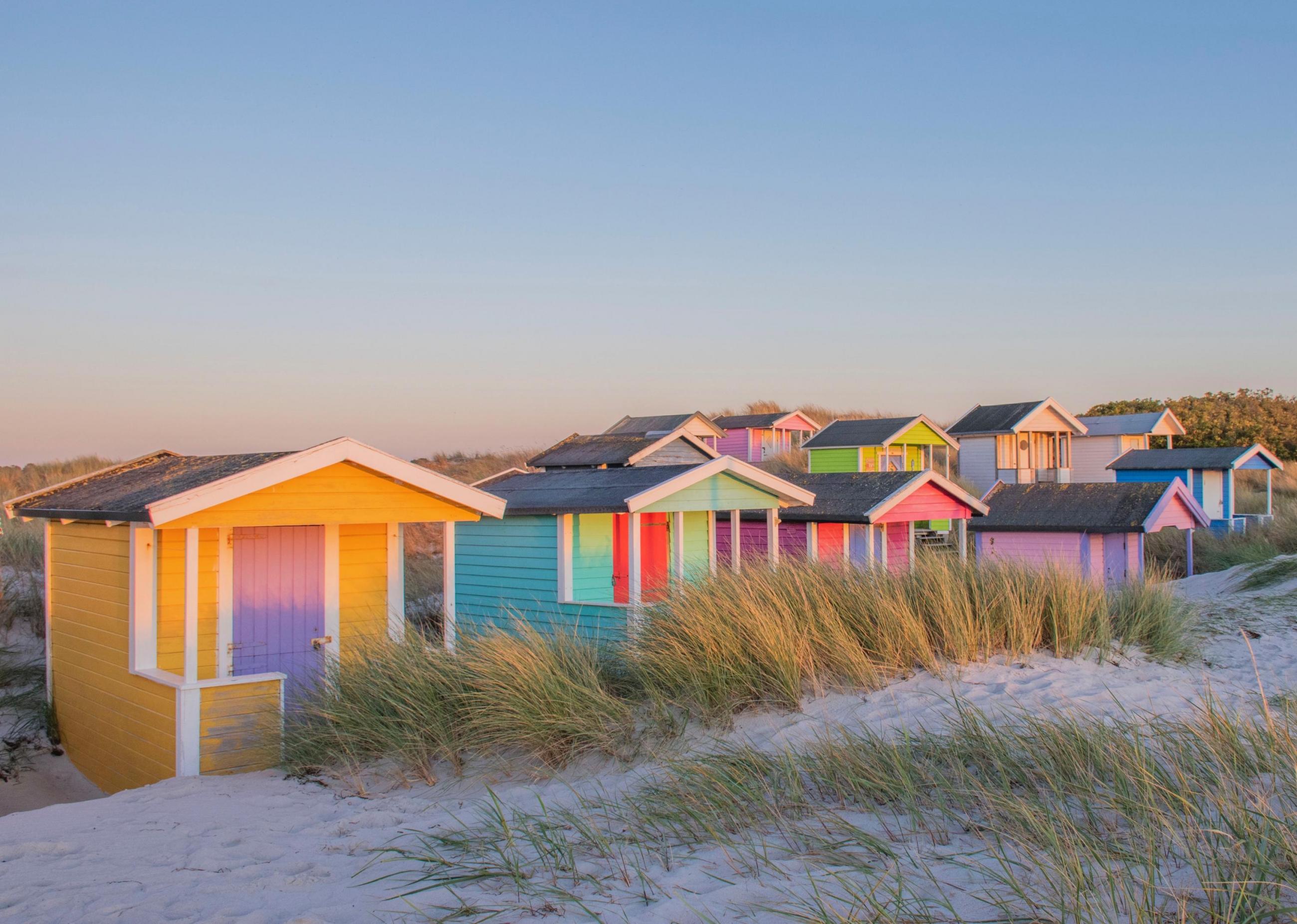 Colorful bathing huts on a white beach under a clear blue sky in Skanör