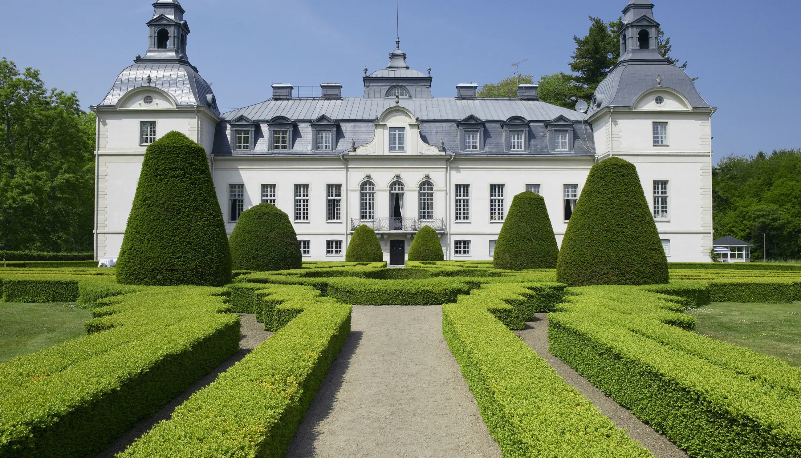 A boxwood garden maze with the fairytale Kronovalls chateaux in the background