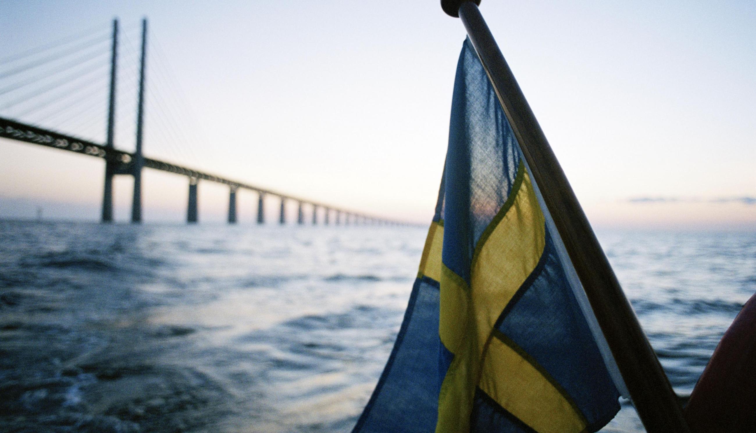 Swedish flag in front of a large bridge in the background