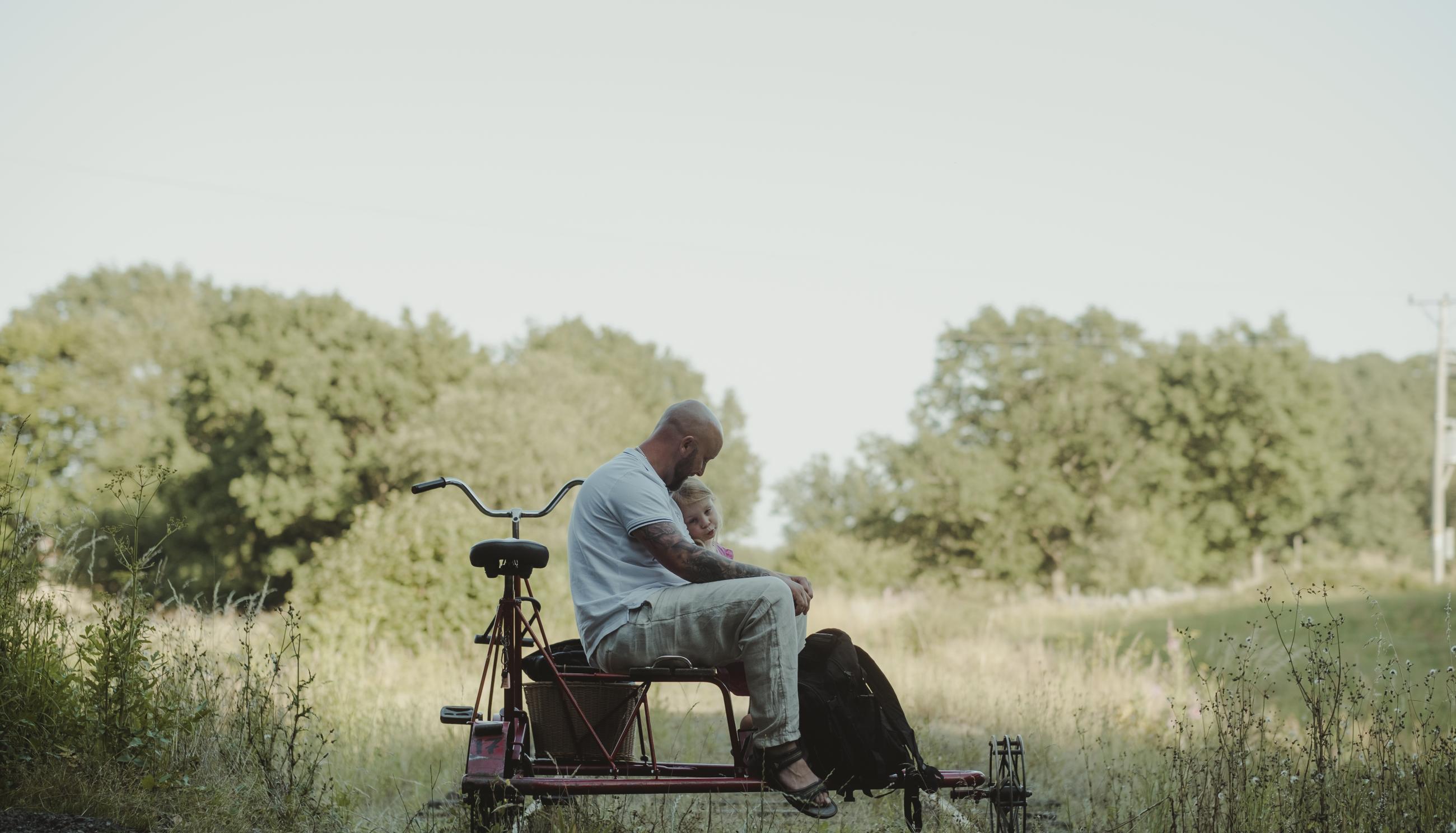 En far sitter tillsammans med sin dotter på en dressin cykel omgiven av naturen