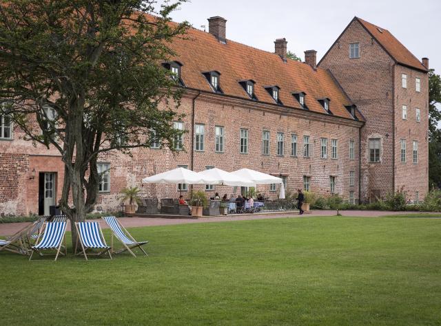 People eating under parasols at the outdoor seating area in the garden infront of Bäckaskog castle
