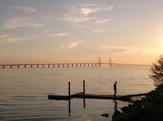 Eine Frau steht bei Sonnenuntergang auf einem Steg und hat die Öresundbrücke im Hintergrund.