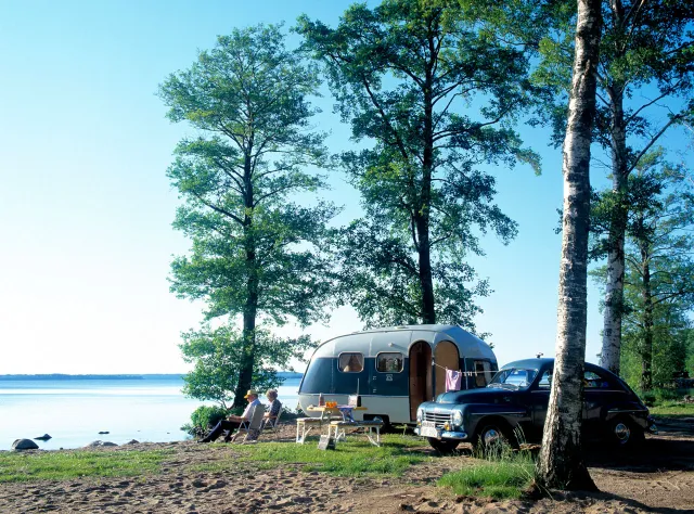 Ein Paar campt mit Auto und Wohnwagen aus den 1940er-Jahren auf dem am See Ringsjön in Skåne.