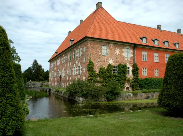 Red brick castle with star pattern on the wall, a moat and green garden